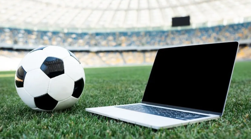 imagem de uma bola num campo de futebol ao lade de um notebook